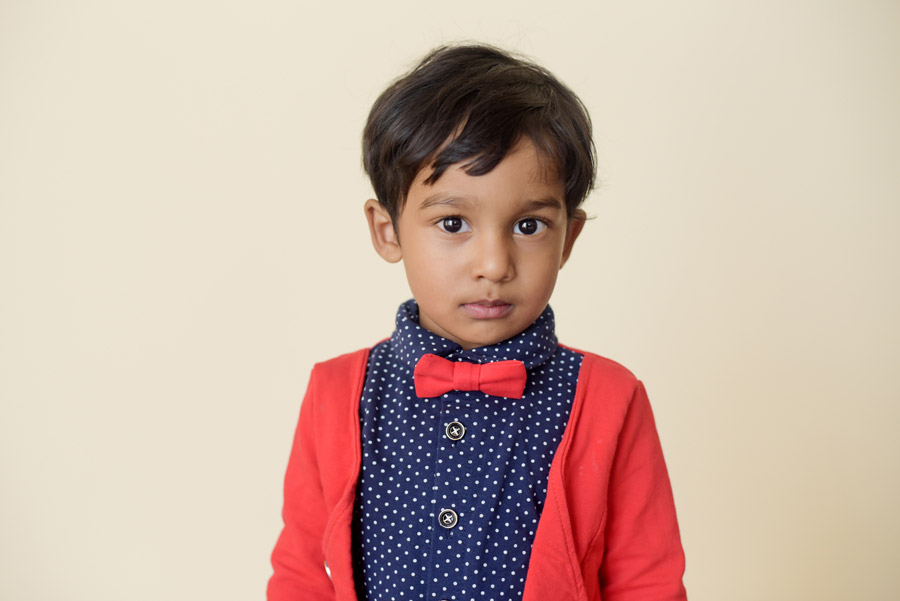 Student dressed up for picture day in a bow tie, polka dot button up shirt and red cardigan. Photographed on a cream backdrop. Photographed by Elizabeth Osberg Photography.