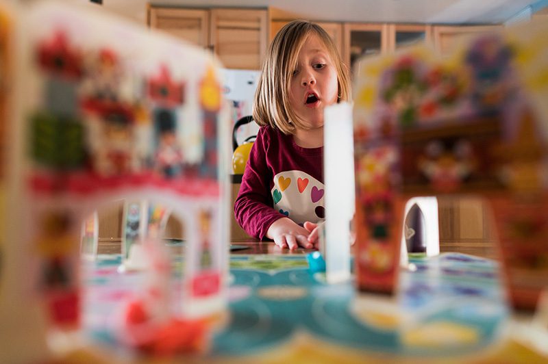 Little girl sitting at kitchen table playing a board game by Denver photographer Elizabeth Osberg