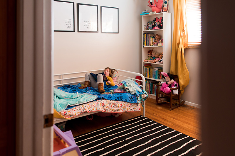 Little girl in her room laying at the end of her bed reading by Denver photographer Elizabeth Osberg