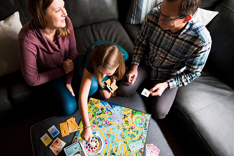 Family of three gathered in living room of home playing the game of Life by Denver photographer Elizabeth Osberg