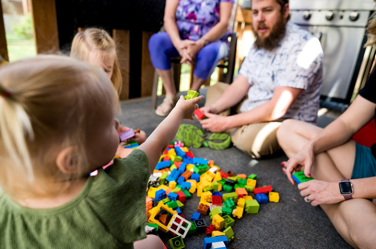 family sitting outside on their deck around a pile of chunky lego blocks playing with lego blocks and talking by denver, colorado documentary photography company real life photo co