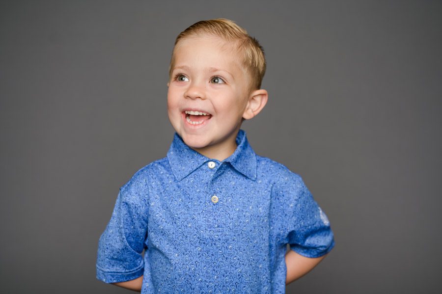 Preschool aged blond boy in a blue polo shirt, photographed on school picture day, with a look of joy on his face.